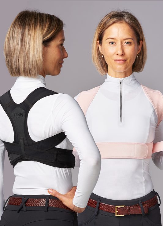 Female wearing dark riding pants, white top and brown leather belt and black posture brace facing side-ways. And again facing forward wearing pink posture brace.
